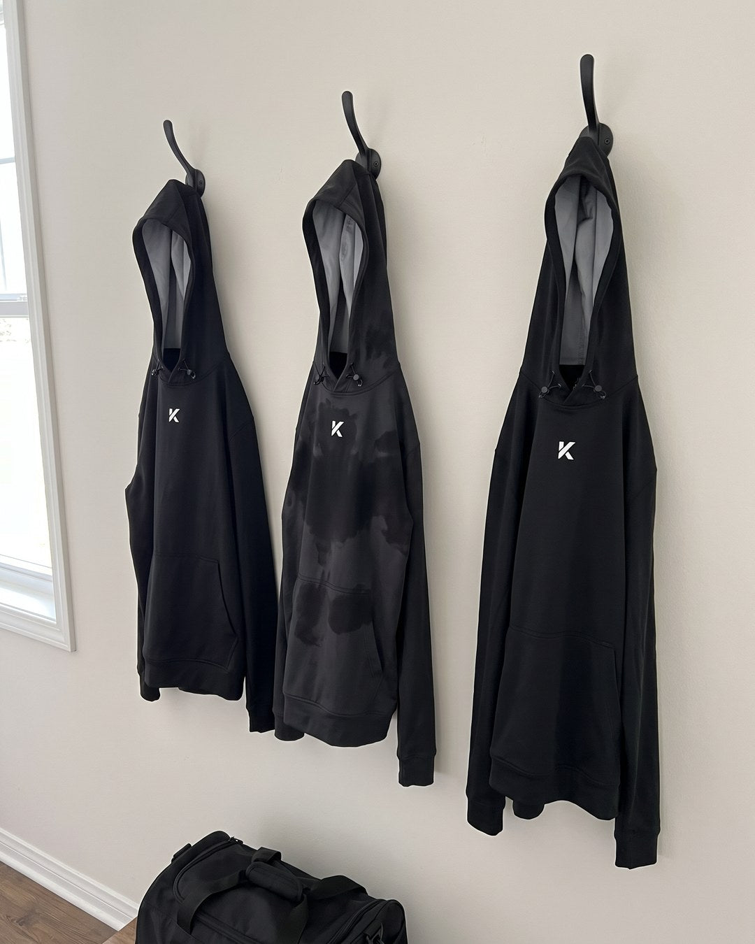 Three black Pro Sauna Hoodies hanging on wall hooks above a gym bag, the middle one soaked and dripping