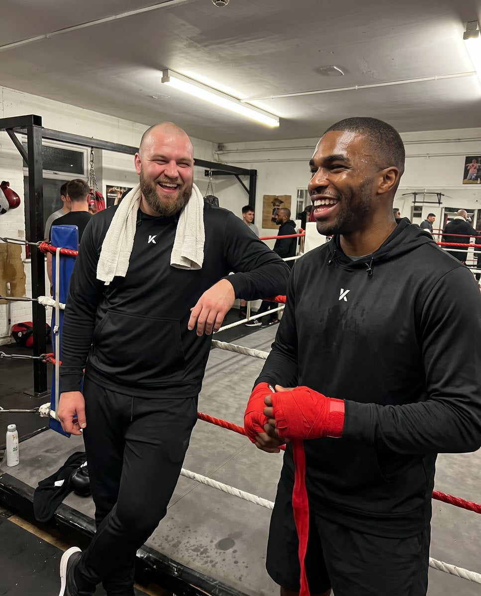 Two men of different builds standing side by side in black Kewlioo hoodies in a boxing gym