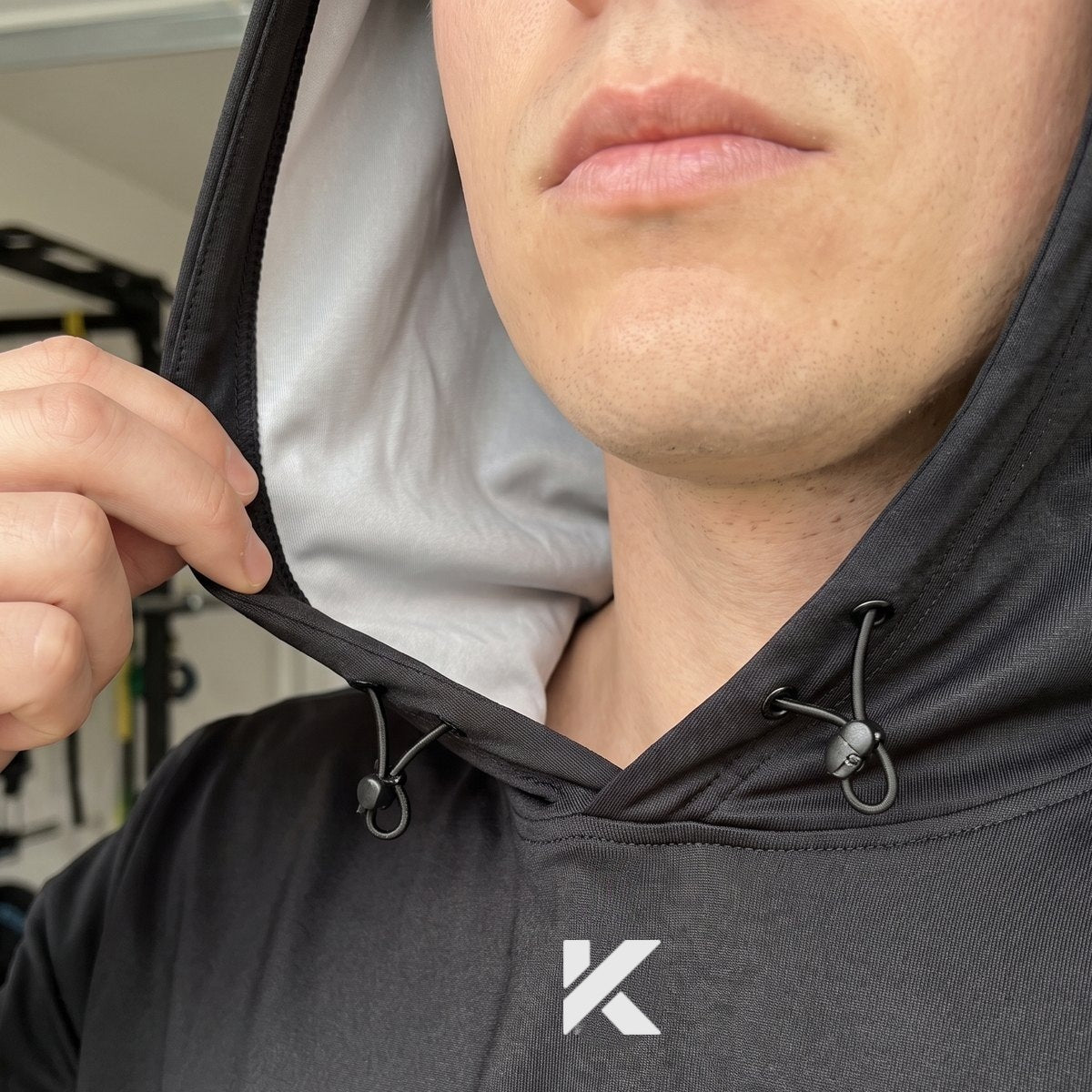 Close-up of a man pulling at the hood of the black Pro Sauna Hoodie, showing the gray lining inside and the drawcords