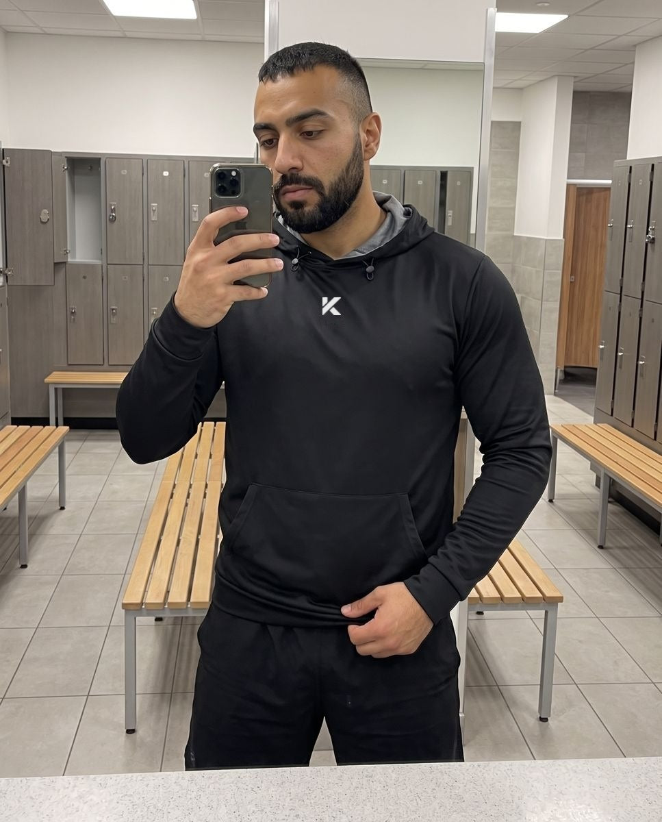 Man in a black Pro Sauna Hoodie taking a mirror selfie in a locker room